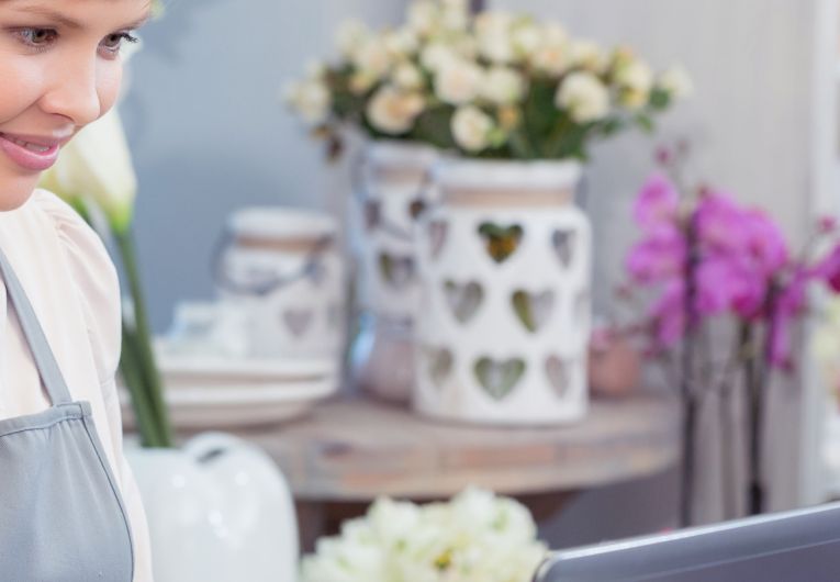 smiling woman in apron works on laptop at flower shop