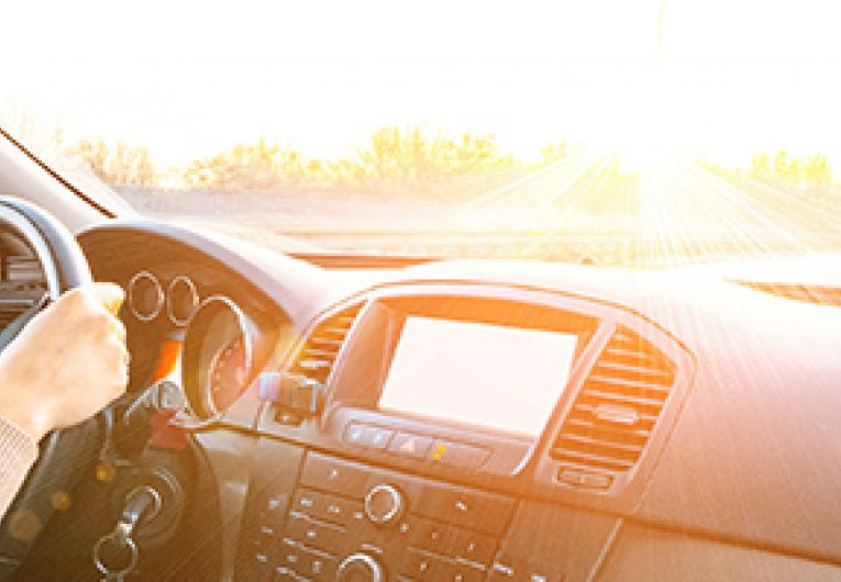 Side profile of a business person driving with both hands on a car's wheel.