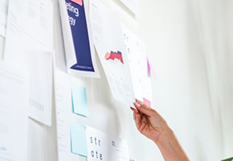 A small business owner reviews customer data pinned onto a large white board.