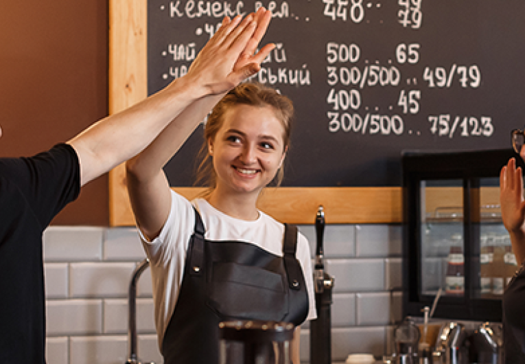 Happy male barista high fiving three female baristas in coffee shop. 