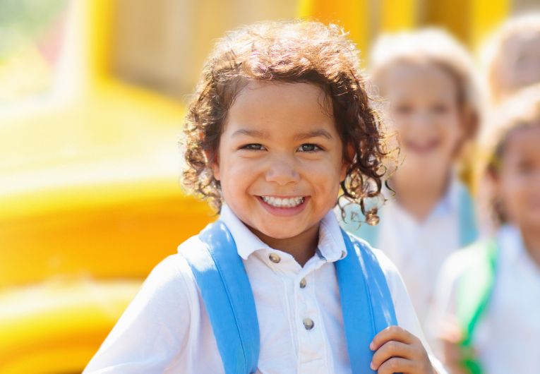 smiling young kids in front of school bus 