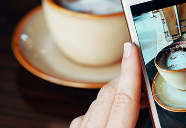 close up of someone using a cellphone with a cup of coffee in the background
