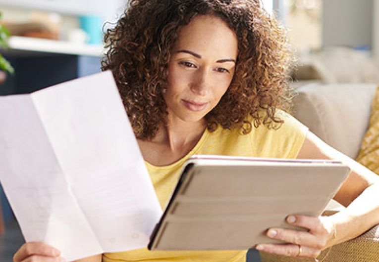 woman comparing the information on a piece of paper to a tablet