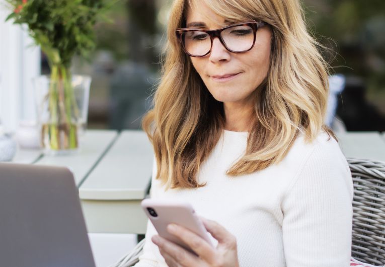 middle age woman works from her pack yard on laptop and phone