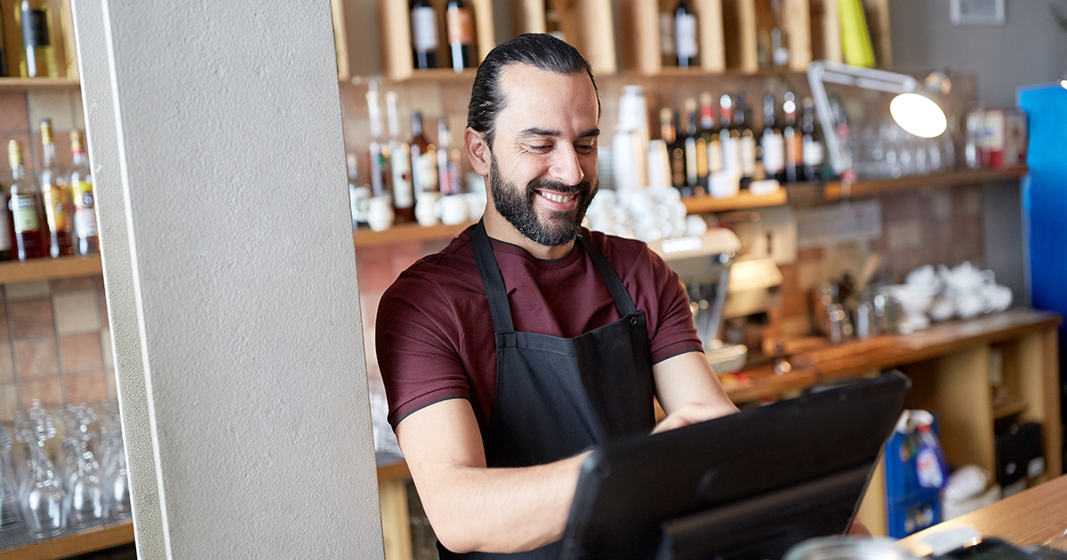 small business owner in apron at counter working at bar or coffee shop on computer