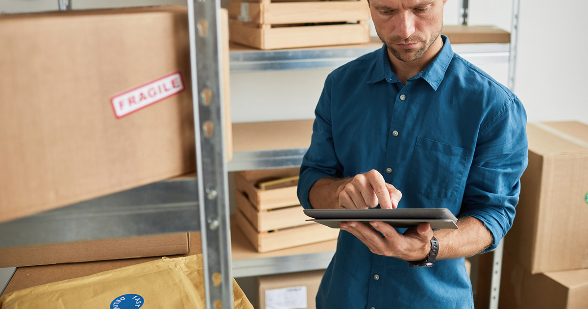 Waist up portrait of young man using digital tablet in warehouse while doing inventory and managing small business