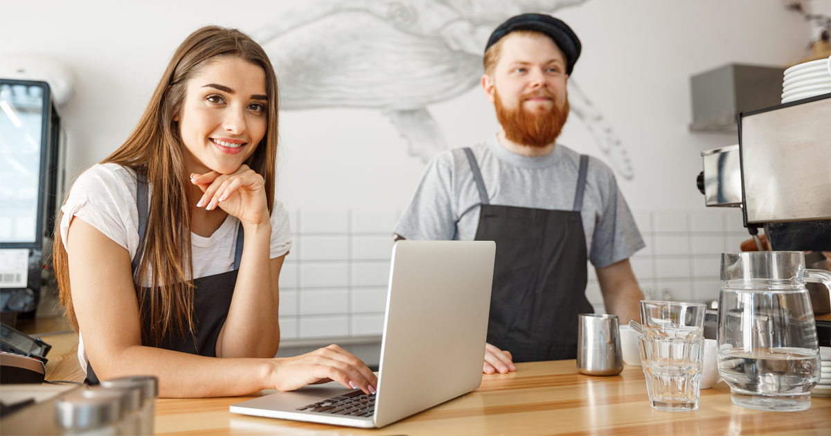 Cheerful baristas working on their laptop in modern coffee shop.