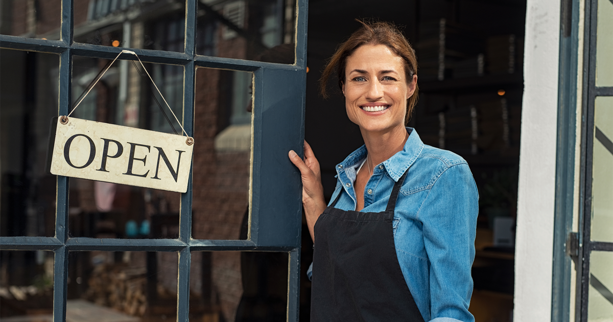 Portrait of a happy waitress standing at restaurant entrance.