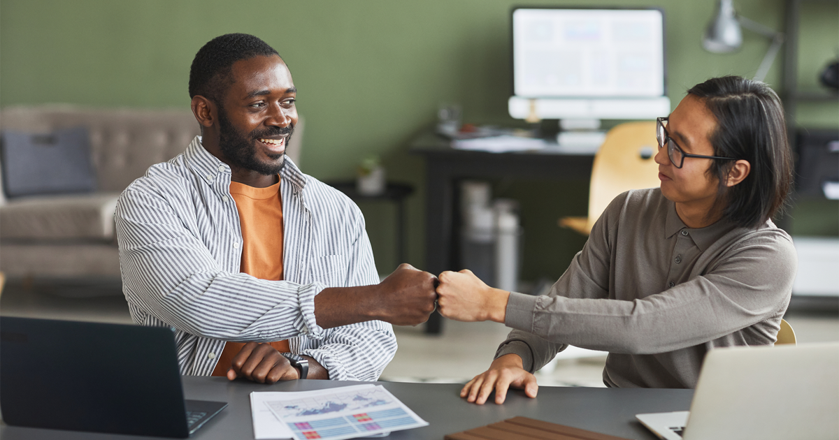 Two businessmen fist bumping while working together in office