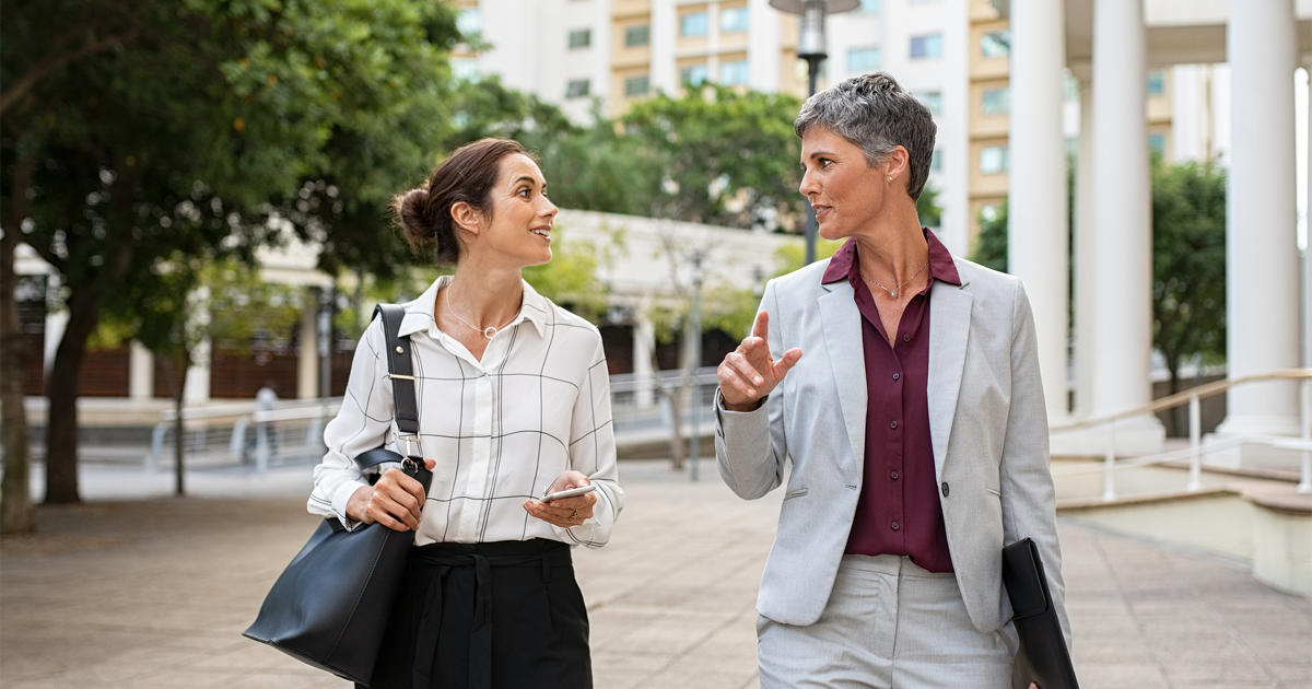 Two business women in conversation walking on city street.