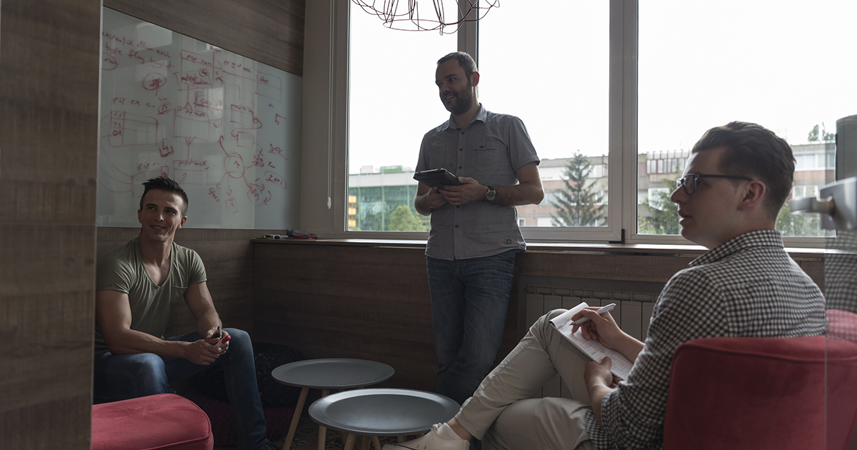 small group of three employees in private office have team meeting and brainstorming while working on laptop and tablet computer