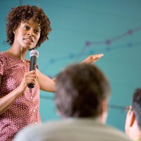 Woman speaking into a microphone to two peers.