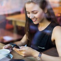 A woman on have smartphone while having coffee.