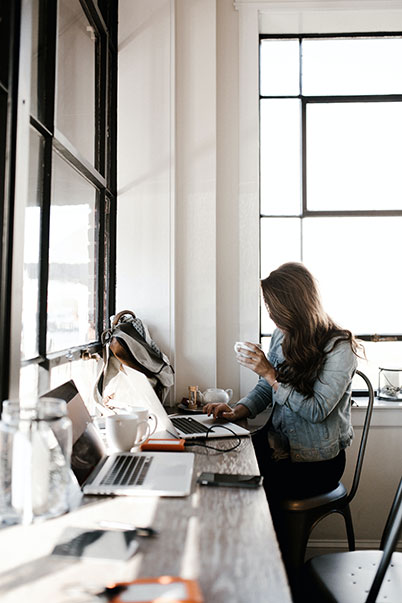 Woman working on laptop while drinking tea.